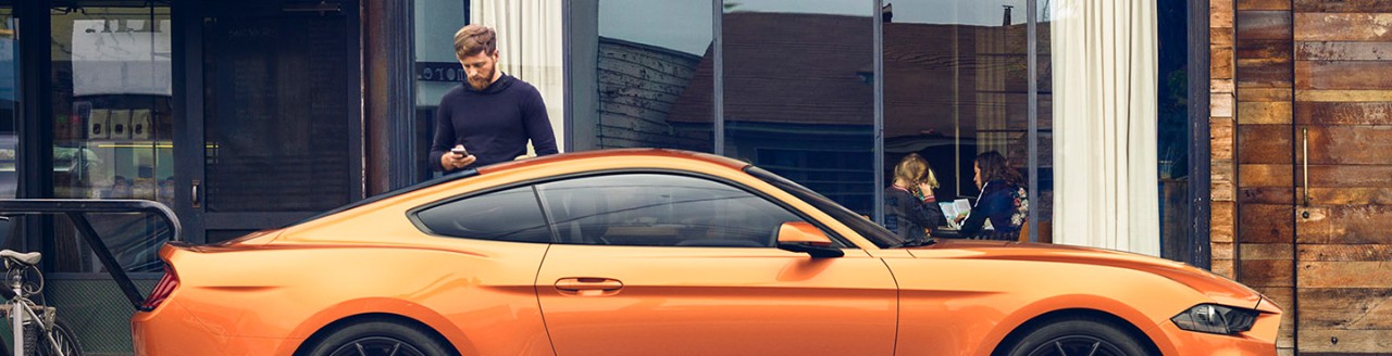 Man standing next to orange Ford Mustang car